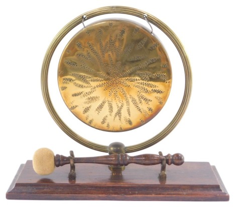 An early 20thC brass table gong, with beater, raised on an oak base, 28cm wide.