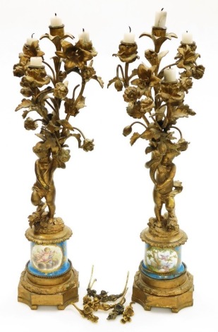 A pair of 19thC French ormolu candelabra, each with four branch candle holders and foliate ornamentation on figural cherub columns, with quality hand painted porcelain collars in the Sevres style, with reserves of cherubs and landscape decoration on a blu