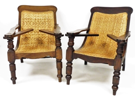 A pair of mid 20thC plantation chairs, each with hardwood frame on wicker rush seat, with tapered column supports and brass buttons, 108cm deep, 62cm wide, 97cm high.