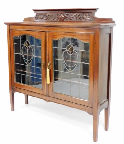 An Art Nouveau mahogany display cabinet, with molded cornice top and fret work detailing, above two leaded stained glass panelled doors with brass handles on tapered legs, 140cm high, 138cm wide, 36cm deep.