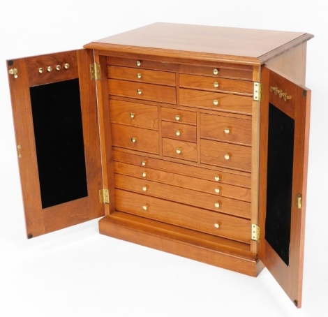 A teak jewellery cabinet, with two single cupboard doors opening to reveal an arrangement of short and long drawers, each with a blue velvet interior, with two keys, boxed, 67cm high, 61cm wide, 43cm deep.