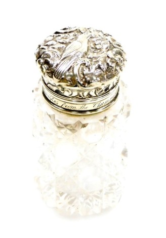 A Victorian silver topped and cut glass scent bottle, the lift up lid with central bird and flower detailing, with glass stopper and pressed glass body with inscription to rim 'With Best Wishes From The Chummerie Xmas 1888', London assay, hallmarks rubbed