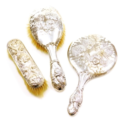 A matched silver backed dressing table set, comprising matching hand brush and mirror with embossed detailing five children's heads, with wings, Chester 1906, and a later cherub designed small brush, London assay. (3)