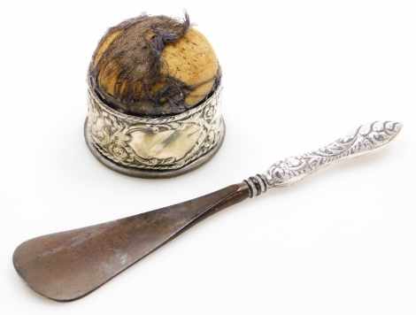 Two items of silver ware, to include a Edward VII silver collared pin cushion, with cherub and floral detailing, the pin cushion rubbed, together with a silver handled shoe horn. (2)