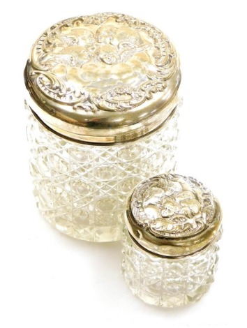 Two George V silver and pressed glass dressing table jars, the silver topped jars each with circular embossed lids of five cherub figures with wings, Birmingham 1924, 9cm and 5cm high. (2)