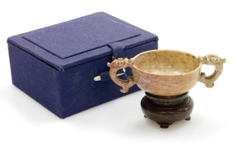 A Chinese carved stone two handled libation cup, with dragon handles, on a hardwood stand, 5cm high, boxed.