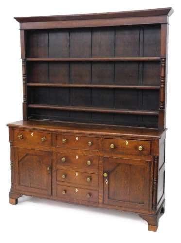 An early 19thC oak and mahogany dresser, the raised back with three plate shelves flanked by part turned pilasters, the base with an arrangement of three frieze drawers and two panel doors, each with brass handles and bone escutcheons, flanked by turned p