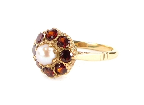 A 9ct gold dress ring, with central raised cultured pearl in pearl setting with arrangement of eight round brilliant cut garnets, with pierced design shoulders, ring size O½, 2.6g all in. (boxed)