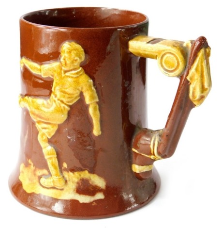 A Dartmouth pottery mug, decorated with a footballer, the handle decorated as a football boot and whistle, 13cm high.