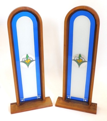 A pair of arched stained glass windows, each mounted in hardwood frames with rectangular bases, 110cm high, 46cm wide.