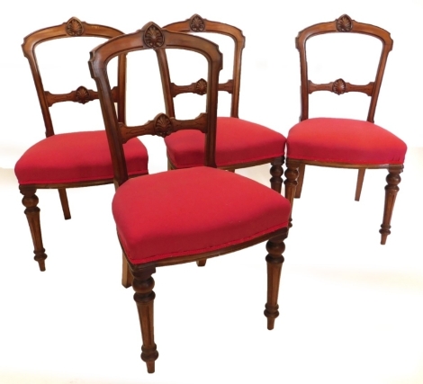 A set of four Victorian walnut balloon back chairs, each with a carved back, a red padded seat on turned fluted legs.