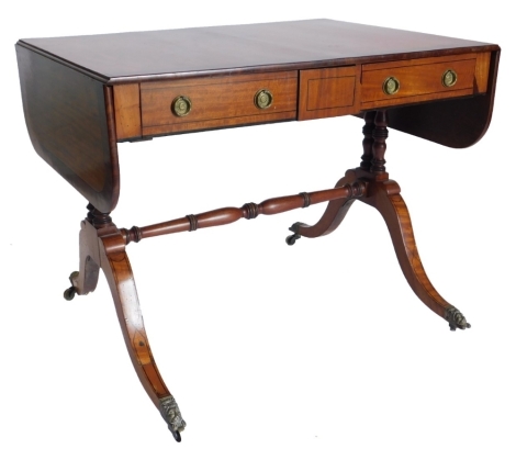 A 19thC satinwood and mahogany sofa table, with ebony stringing, the rectangular top with rounded ends, above two frieze drawers, each with ring handles on twin turned end supports with stretcher, with splayed legs and brass lion mask handles, 71cm high, 