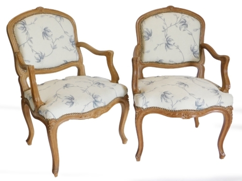 A pair of French style hardwood fauteuil, each with a moulded frame, upholstered in blue and cream floral fabric on cabriole legs. The upholstery in this lot does not comply with the 1988 (Fire & Fire Furnishing) Regulations, unless sold to a known export