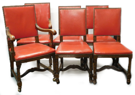 A set of six oak dining chairs, each with a red leather padded back and seat, with brass studded borders on spirally turned legs, with H stretcher, two with arms.