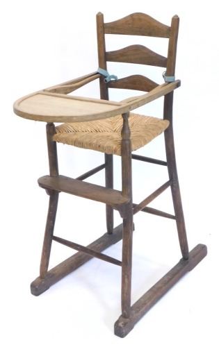 An early 20thC country made oak and ash ladder back child's high chair, with a rush seat on turned supports.