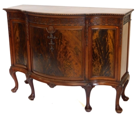 A mahogany bowfronted side cabinet, the top with a carved border above a blind fret frieze, and a central figured door carved with shells etc, flanked by further panels, with a moulded frieze carved with shells on cabriole legs and pad feet. 92cm high, 12