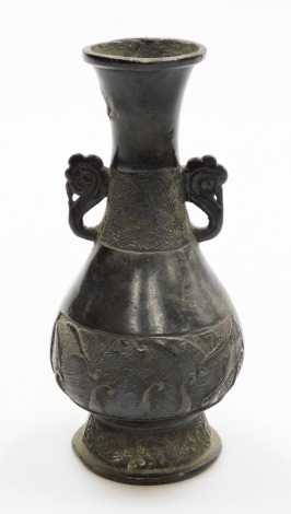 A Chinese bronze vase, on flared foot, with everted neck and two ear handles, the low relief decoration of diaper and wave designs, 19thC or earlier, 20cm high.