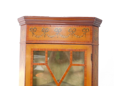 An Edwardian Sheraton Revival satinwood and painted corner display cabinet, painted with floral swags and bows, and interlocking trails of hare bells, the outswept pediment over a glazed door, enclosing two shelves, above a cane paneled door, set with a p - 2