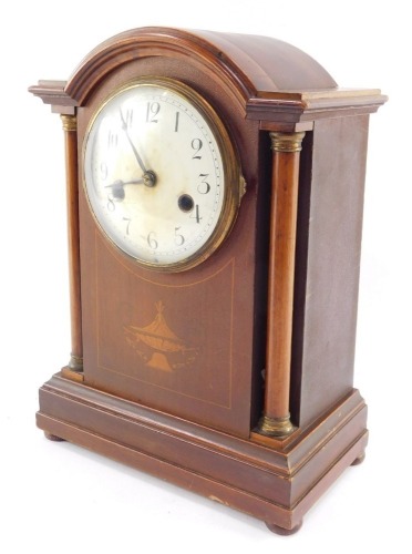 A late Victorian mahogany and inlaid mantel clock, circular enamel dial bearing Arabic numerals, German eight day movement, with coil strike, the case of domed architectural form, with brass capped columns, raised on a plinth base, on bun feet, with pendu