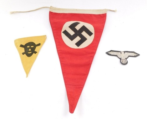 A Third Reich Swastika car pennant, red ground, 32cm wide, a WWII SS Uniform badge, and a Poison Gas pennant, showing a skull and crossbones, against a yellow ground. (3)