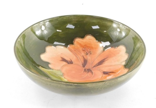 A Moorcroft pottery dish decorated in the Coral Hibiscus pattern, against a green ground, impressed marks, 14cm diameter.