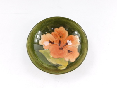 A Moorcroft pottery dish decorated in the Coral Hibiscus pattern, against a green ground, impressed marks, 14cm diameter. - 2