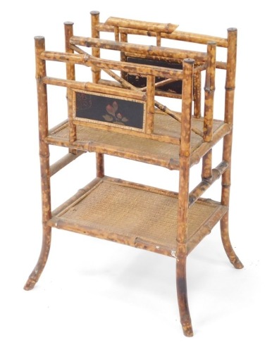 A Victorian Aesthetic period bamboo Canterbury whatnot, with inset lacquered panels, with a twin division cane bottomed upper tier, over a further cane set shelf, raised on out swept legs, 72cm high, 47cm wide, 39cm deep.