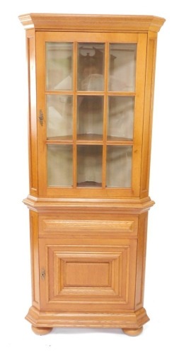 An oak standing corner cabinet, with a single glazed door, above a paneled door, on bun feet, 182cm high, 76cm wide.