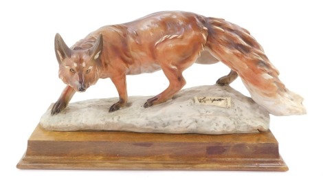 A Florence Capo di Monte porcelain figure of a fox, raised on a naturalistic base, with scroll bearing artist's name, on an oak plinth base, 35cm wide.