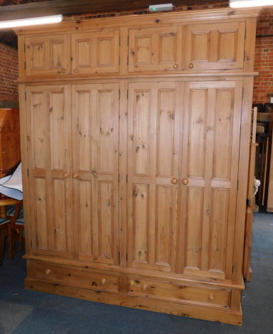 A pine quadruple wardrobe, the out swept pediment over two pairs of doors, opening to reveal two hat cupboards, over four doors, opening to reveal a hanging rail, above two further drawers, raised on a plinth base, 234cm high, 194cm wide, 61.5cm deep.