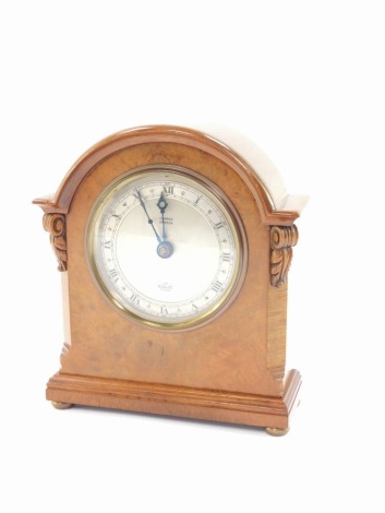 An Elliott walnut cased mantel clock for Hopper of Boston, circular silvered dial with chapter ring bearing Roman numerals, clockwork movement, the domed case with carved foliate detailing, raised on a stepped base, on brass bun feet, 18cm high, 15.5cm wi