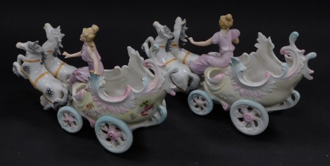 A pair of continental late 19thC porcelain carriage ornaments, each depicting female figures seated on chariot with two horses, 25cm wide.