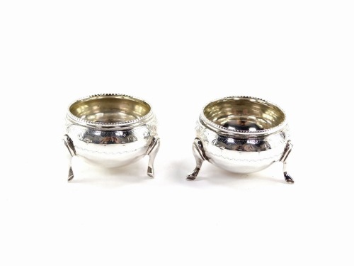 A pair of Victorian miniature circular silver salts, with a reeded collar and hammered detailing with vacant cartouche, on tripod feet, Sheffield 1876, 3.5cm high, 2½oz.