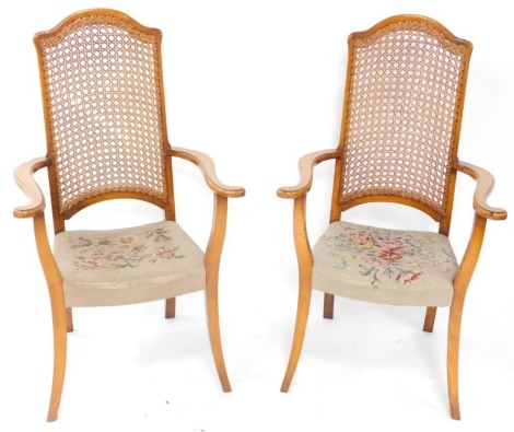 A pair of beech open armchairs, each with a caned back, shaped arms and a wool work seat on splayed legs.