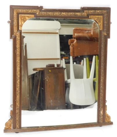 An early 20thC wood grain and parcel gilt over mantel mirror, decorated with foliate scrolls, on bun feet, 109cm high, 100cm wide.