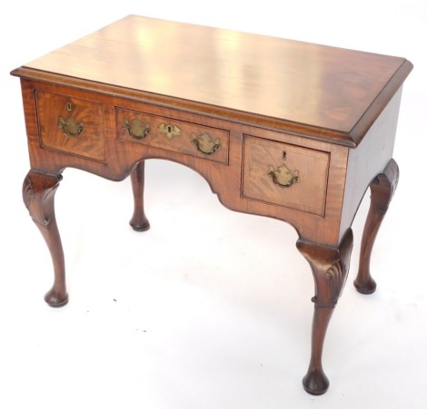 A walnut low boy or dressing table, the cross banded top with a moulded edge, above three frieze drawers, each with brass drop handles, on shell carved cabriole legs with pad feet, 75cm high, 90cm wide, 54cm deep.