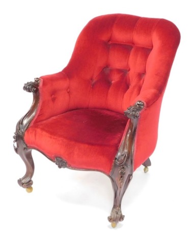 A Victorian rosewood nursing chair, upholstered in red button back velour, raised on cabriole legs, and scroll feet, with floral and foliate carving, on later castors.