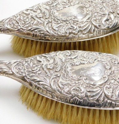 A Victorian silver backed dressing table set, each with heavy foliate scroll detailing with cherubs, bearing the initials MR, comprising two hand brushes, London 1901, two smaller brushes London 1902 and two silver topped glass dressing table jars, London - 3