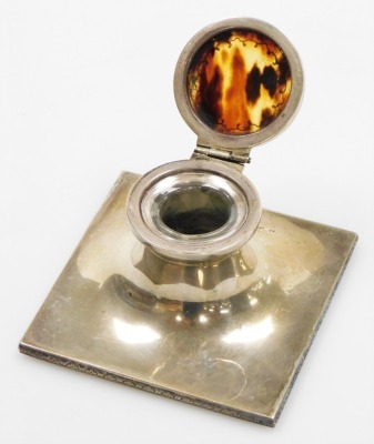 A George V silver and tortoiseshell inkwell, the circular inkwell top with tortoiseshell inlay and applied silver detailing, with a glass inset inkwell on a square base with foliate design border, maker Adie Bros Ltd, Birmingham 1925, 5.5cm high, on a wei - 2