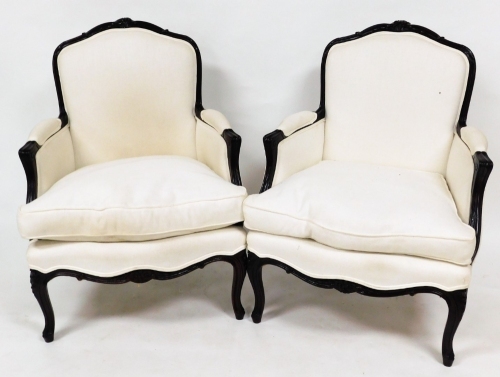 A pair of French style armchairs, with scroll fluted carved arms and cabriole legs, upholstered in a white woven material.