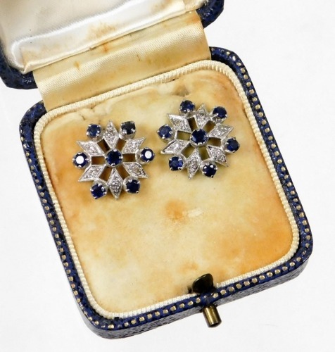 A pair of sapphire and diamond cluster earrings, each with round brilliant cut sapphire in claw setting with illusion set tiny diamonds, in star type detailing, in white metal, unmarked, possibly white gold, in a Oclee & Son of Folkestone fitted case, 4g