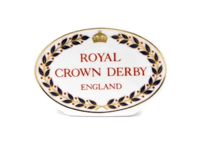 A Royal Crown Derby retailers' plaque, oval with red Royal Crown Derby England stamp to centre, 10.5cm wide.