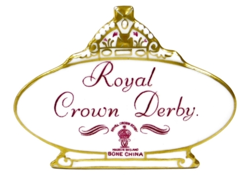 A Royal Crown Derby retailers' plaque, with crown top on an oval plaque with purple stamp and writing, 10cm wide.