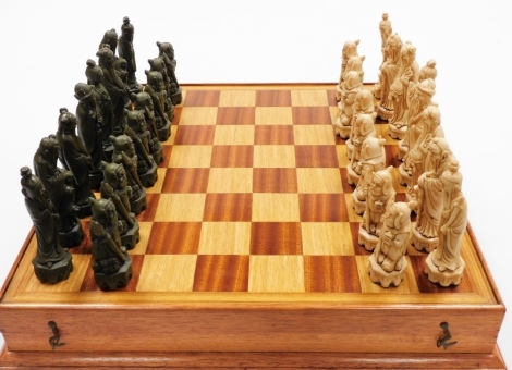 An oriental resin chessboard and chess pieces, the pieces each of oriental figures in white and green, with a beech chessboard 7.5cm high, 47cm wide, 47cm deep.