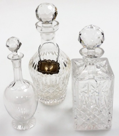 Three pressed glass decanters, to include two pressed glass decanters, one of circular, the other square, each with stopper and a moulded glass decanter early 19thC, together with a silver port label, London 1973, 29cm, 14.5cm and 27cm high. (3)