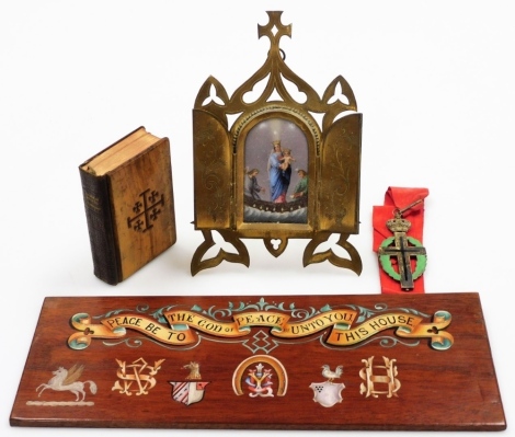 A group of religious ephemera, to include a 'peace be to the god of peace be unto you this house' plaque, a book of common prayer and hymns with treen cover, a brass framed porcelain portrait plaque depicting Mary and Jesus, and an enamelled and brass cru