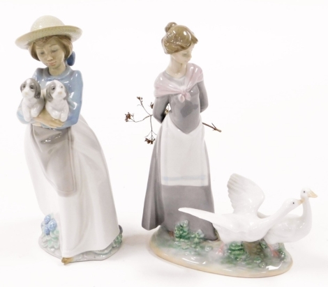 A Lladro figure of a lady and two geese, 24cm high, and a Nao figure of girl carrying two puppies, 24cm high. (2)