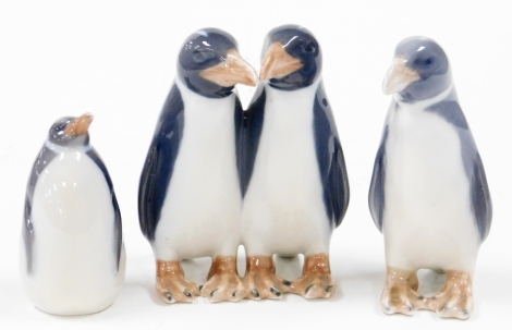 A group of Royal Copenhagen penguins, to include a figure group of two, 10cm high, a single walking penguin, 10cm high, and a further seated penguin, 7cm high. (3)