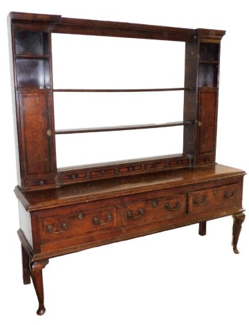 A George III oak dresser, with plate rack top centred above two open sections and single door and drawer side, with five small drawers to the centre, on a base with three drawers, on cabriole legs, with brass handles, 196cm high, 185cm wide, 51cm deep.