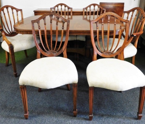 A mahogany dining room suite, comprising a twin pedestal dining table, with additional leaf and marquetry outer banded border, 77cm high, 144cm wide, 99cm deep, together with a set of six chairs, two carvers, each with shield back on a cream floral uphols